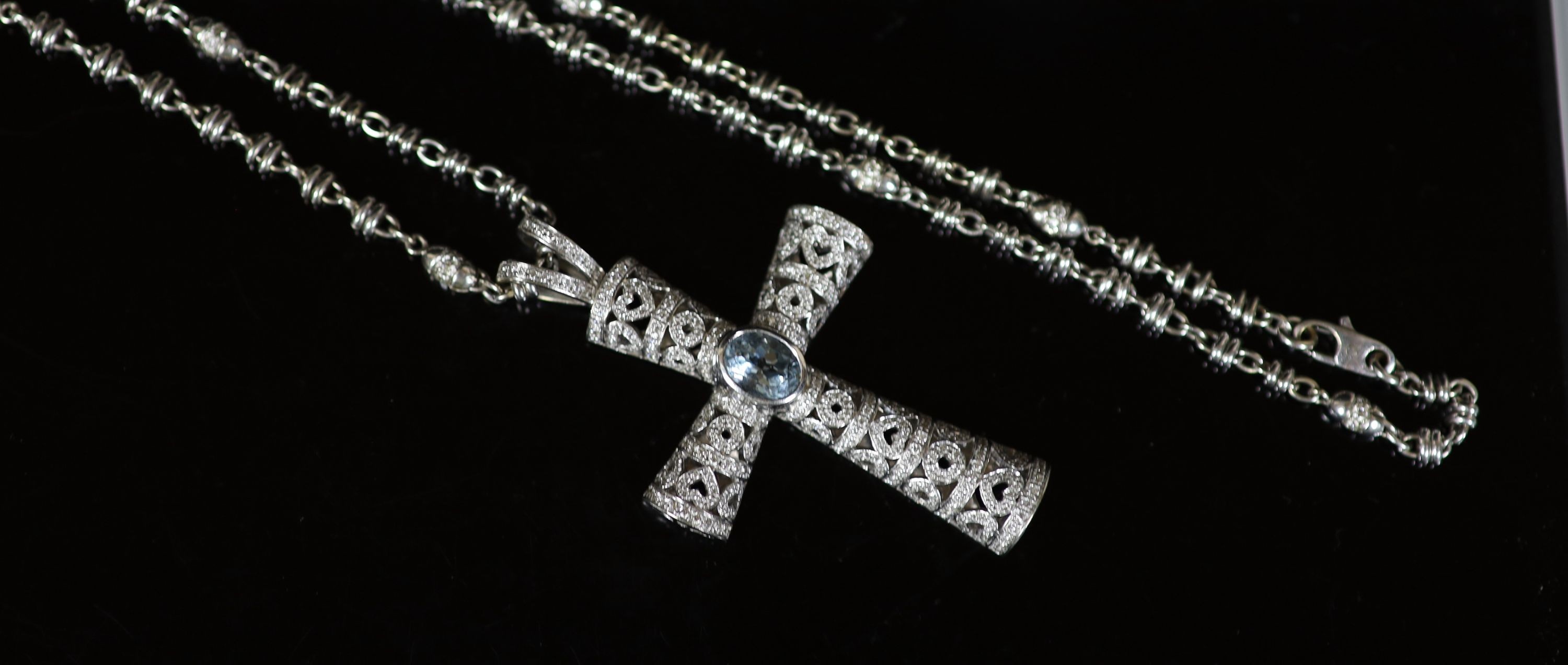A Theo Fennell white gold, oval cut aquamarine and diamond chip cluster set pierced cross pendant, on a white gold and diamond set chain